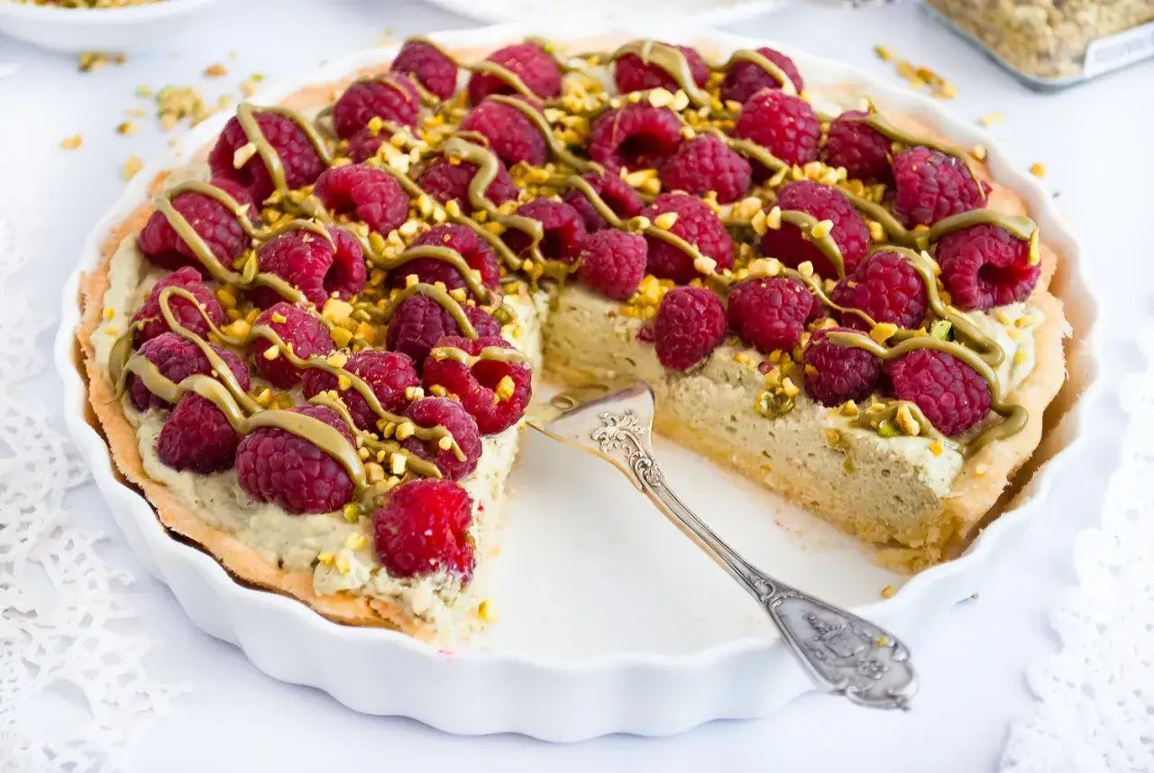 Pyszna tarta pistacjowa z malinami i posypką z pistacji, udekorowana zielonym kremem. Wygląda apetycznie!