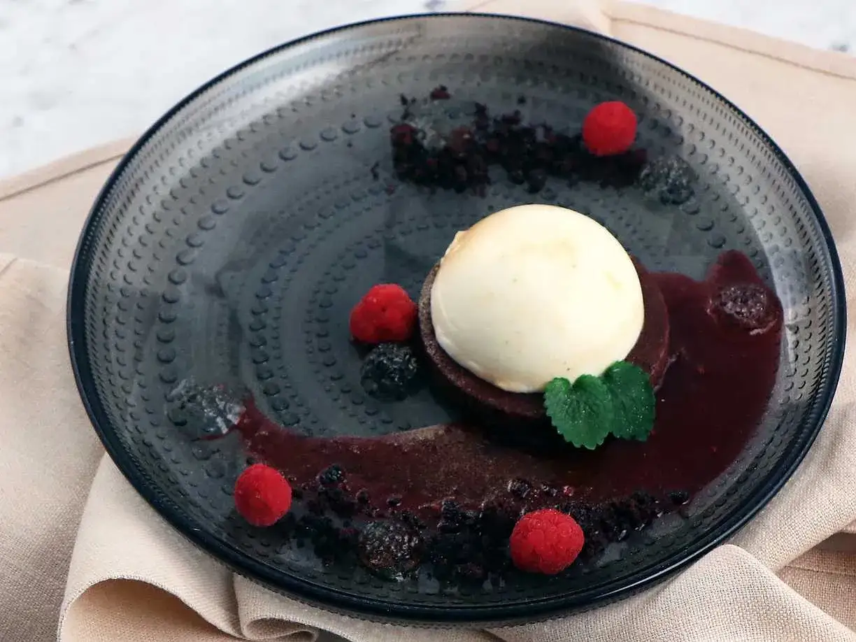 En elegant dessert till ny&aring;r: chokladkaka med vaniljglass, b&auml;rs&aring;s och f&auml;rska hallon p&aring; en m&ouml;rk tallrik.