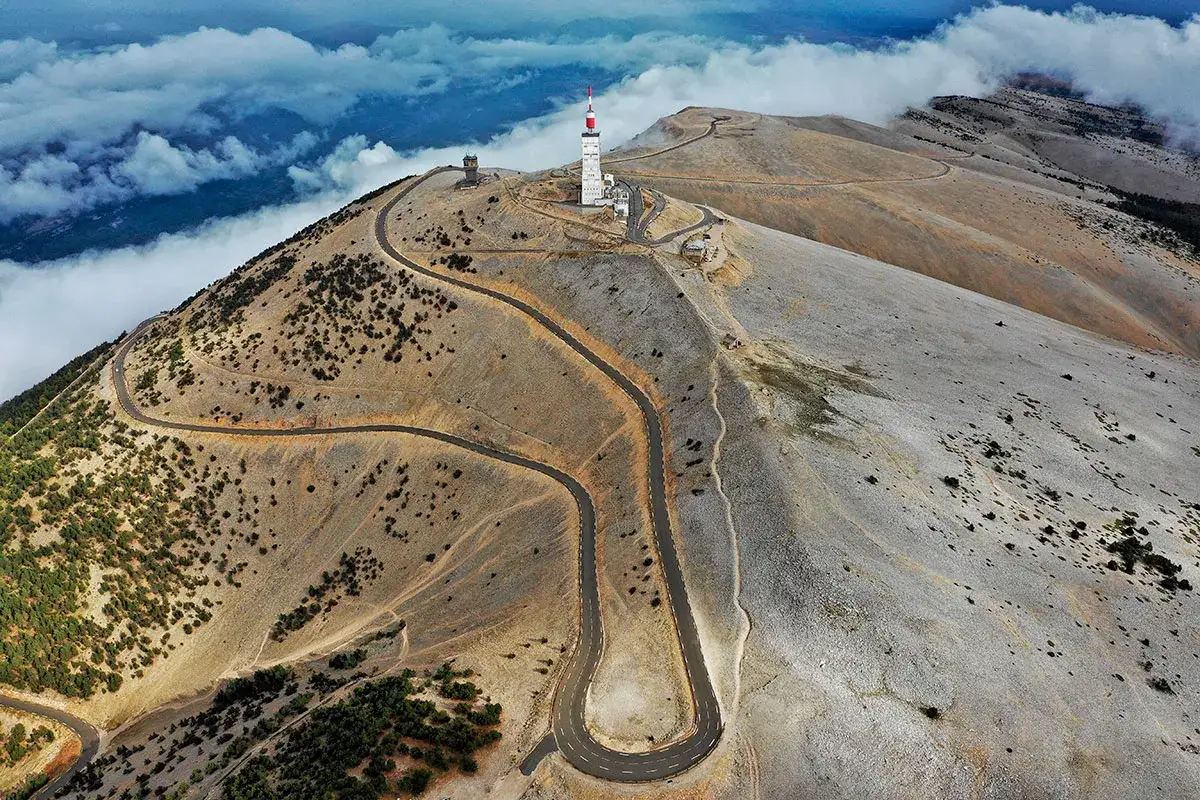 Vue a&eacute;rienne du **tour du Mont Ventoux**, avec ses lacets sinueux serpentant sur le flanc aride, domin&eacute; par une tour de t&eacute;l&eacute;communication.
