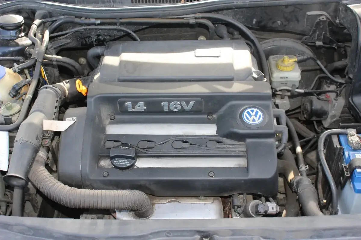 Silnik 1.4 16V w Volkswagen Golf 4. Widoczny jest czarny plastikowy kolektor, logo VW i elementy układu dolotowego.