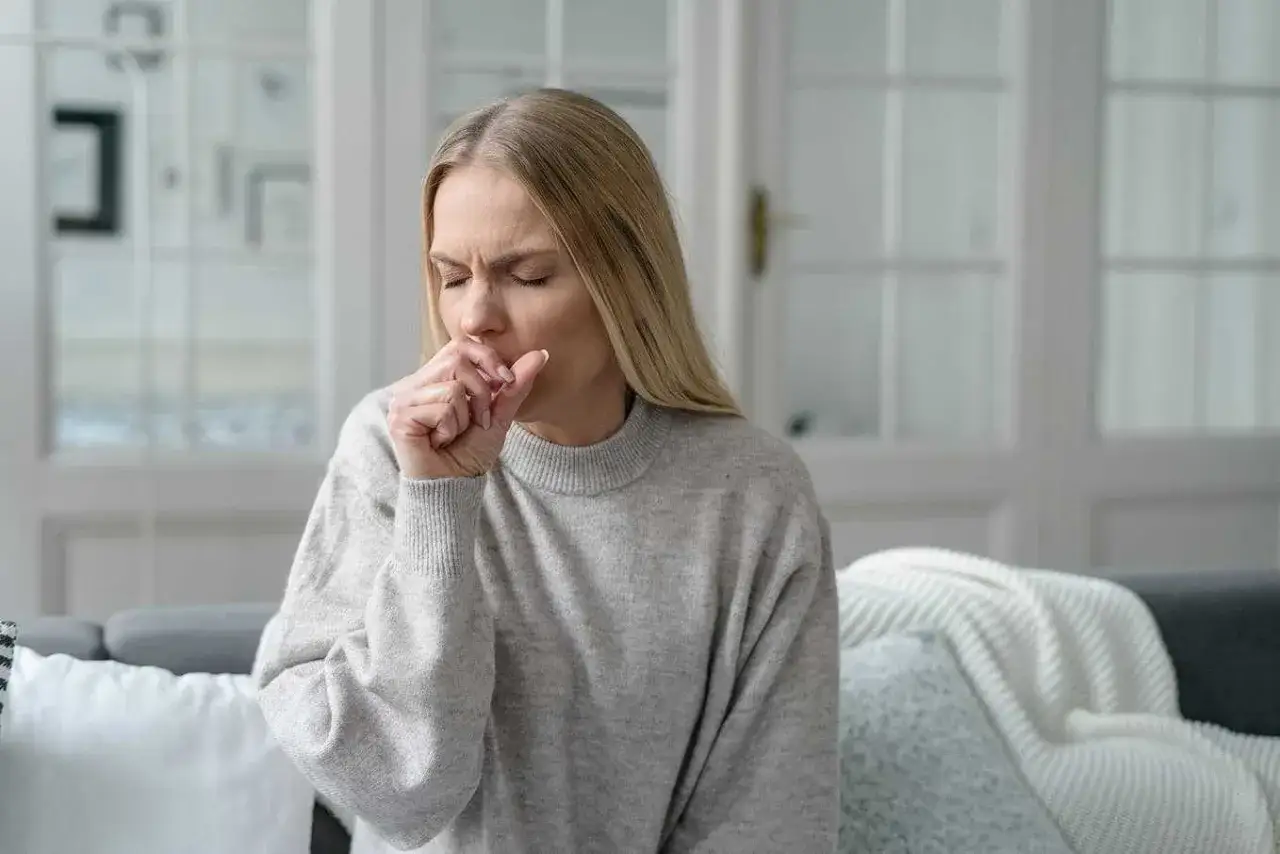 Kvinna med blundade &ouml;gon hostar i handen, s&ouml;ker lindring fr&aring;n hosta.