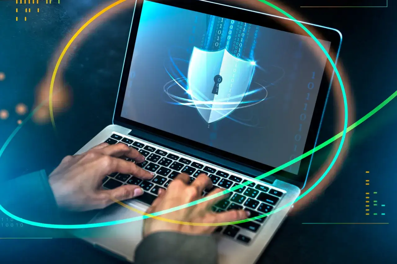 Osoba pisze na laptopie, na ekranie którego widnieje tarcza z kluczem i kod binarny. To symbol bezpieczeństwa, jak token CSRF chroniący przed atakami.