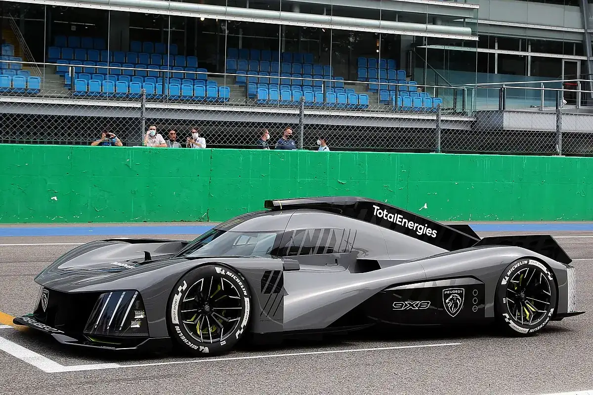 Futurystyczny Peugeot 9X8 na torze wyścigowym, z widownią na trybunach w tle.