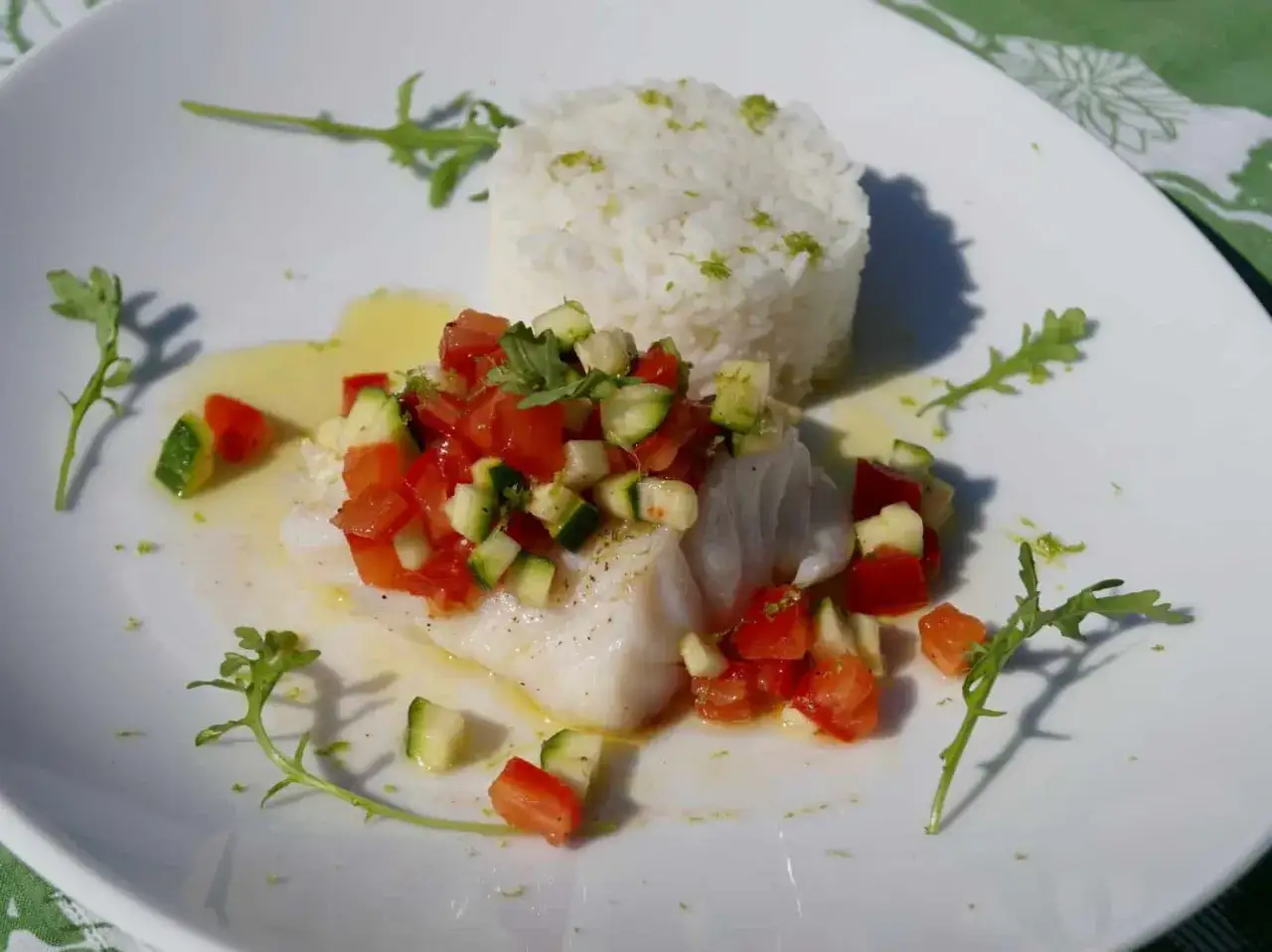 Poisson blanc servi avec du riz et une sauce vierge aux tomates et concombres, garni de roquette.