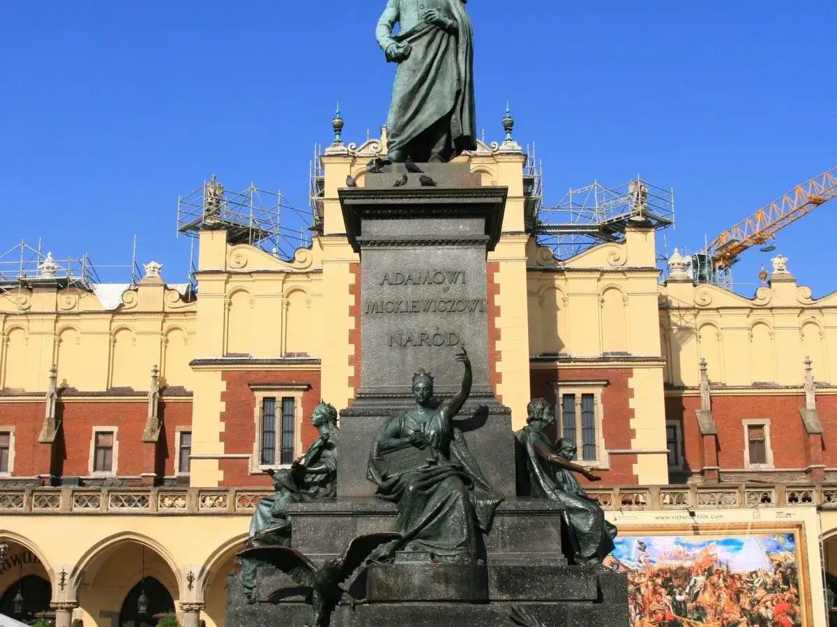 Pomnik na rynku w Krakowie upamiętnia Adama Mickiewicza. W tle Sukiennice, a nad nimi rusztowania i dźwig.
