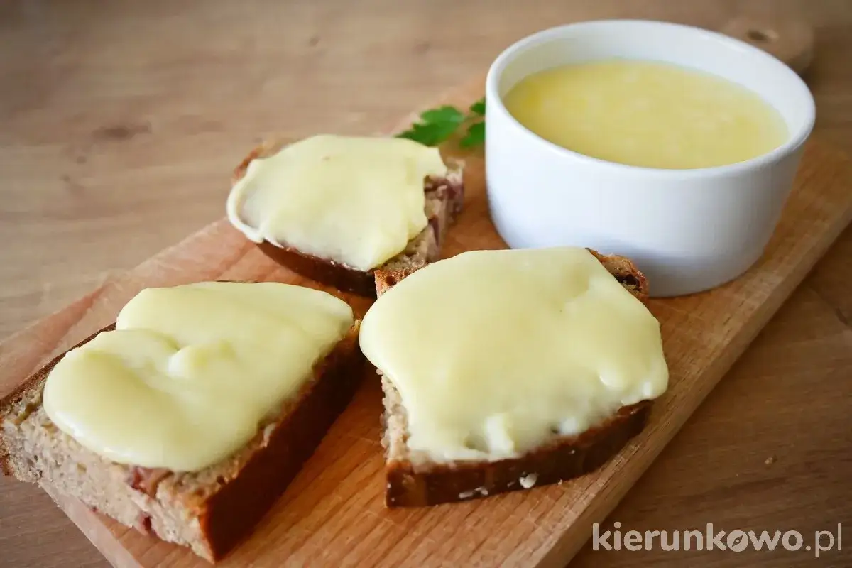 Chcesz wiedzieć, jak zrobić ser z mleka? Na desce leżą kromki chleba z rozpływającym się serem i miseczka z płynnym serem.