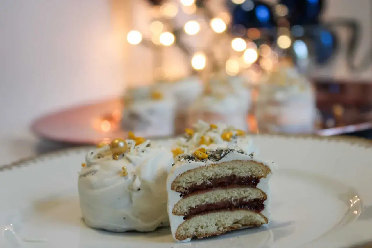 Sm&aring;, vita bakelser med syltfyllning och gulddetaljer, perfekta som elle ny&aring;rsdessert. Bakgrunden &auml;r mjukt suddig med ljus.
