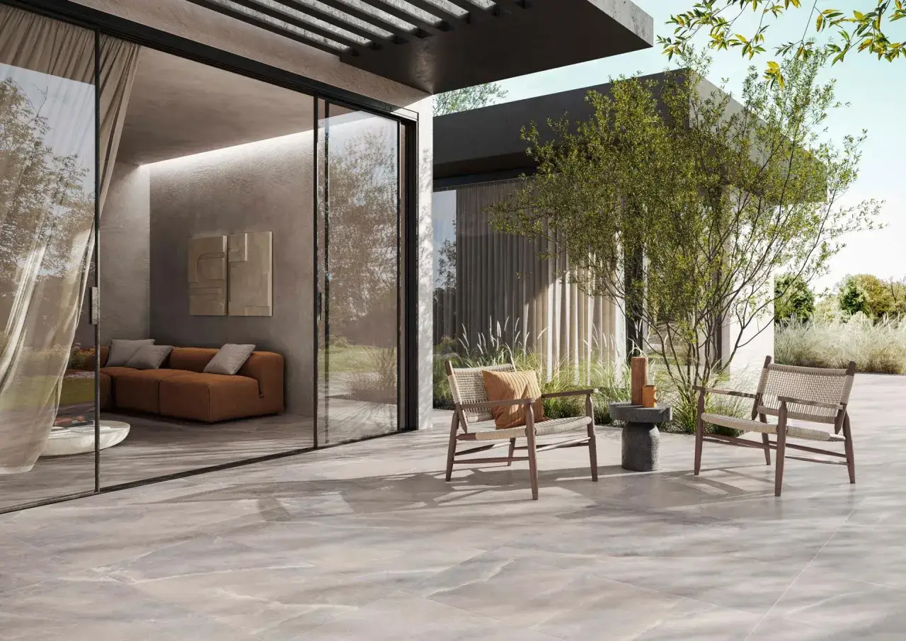 Posa gres porcellanato effetto pietra per un patio moderno con divano, sedie e vegetazione rigogliosa.
