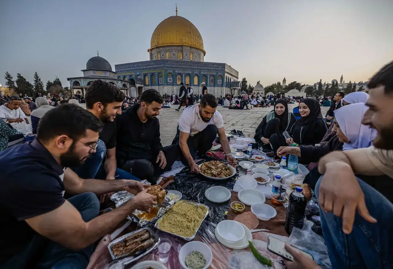 Rodzina i przyjaciele dzielą się posiłkiem iftar co to, siedząc na kocu przed Kopułą na Skale.