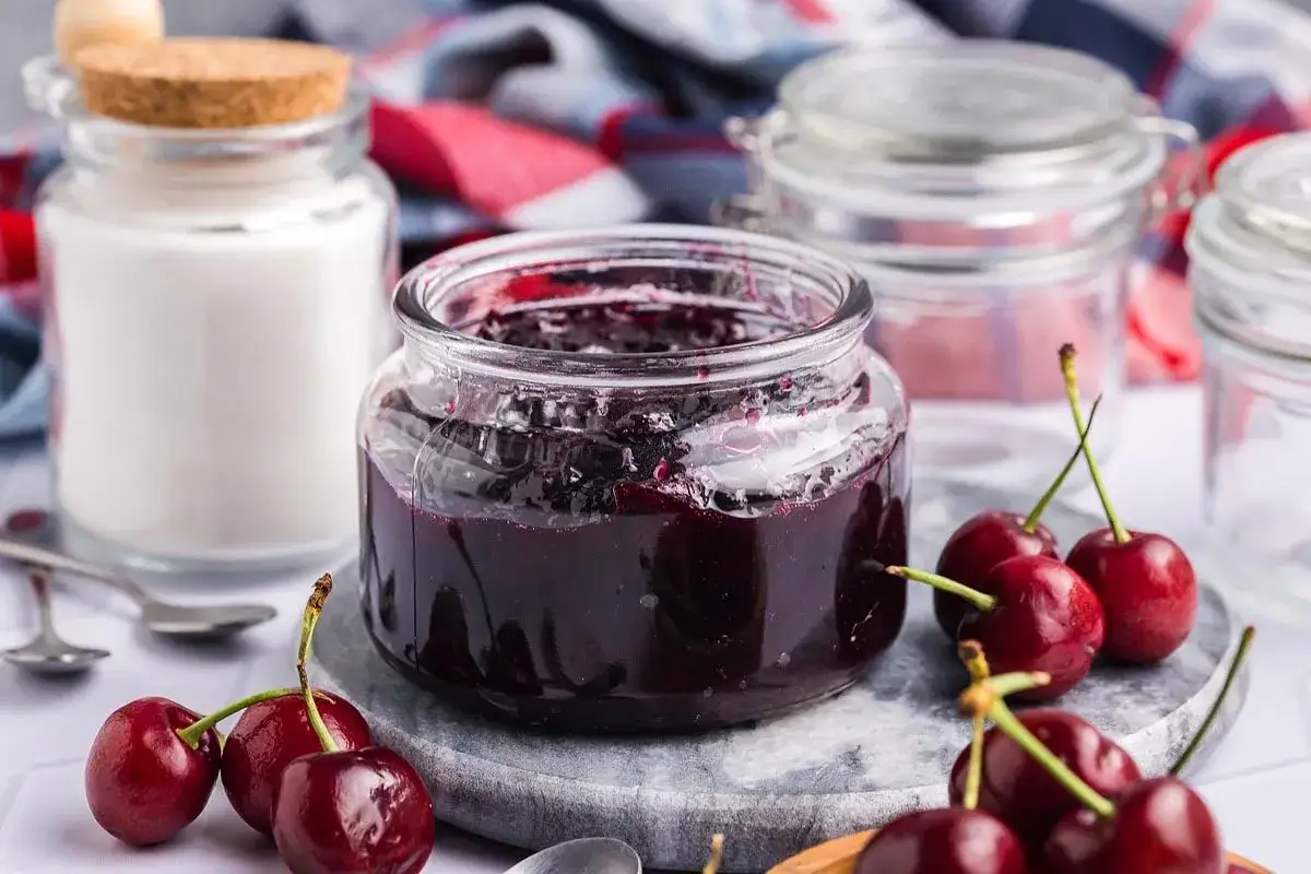 Confiture de cerises maison dans un bocal, avec des cerises fra&icirc;ches et du sucre &agrave; proximit&eacute;. Une belle id&eacute;e pour comment conserver des cerises.