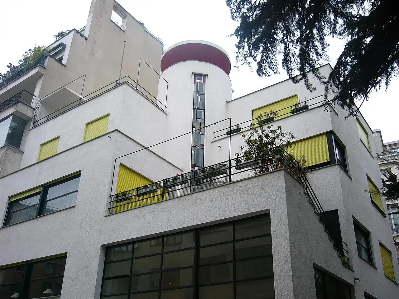 Bâtiment blanc aux lignes géométriques, volets jaunes et balcon fleuri, rue Mallet Stevens.