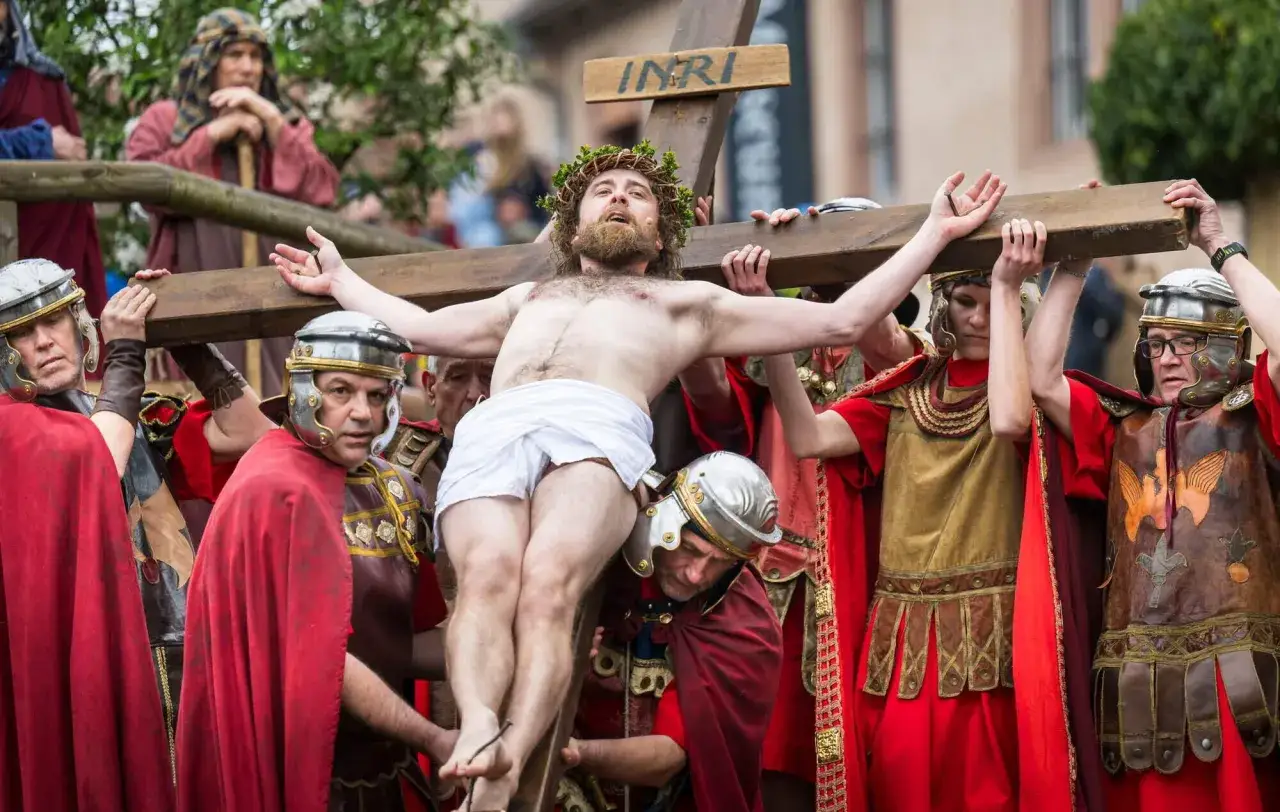 Darstellung der Kreuzigung Christi, die die Karwoche Bedeutung verdeutlicht. Männer in römischen Kostümen tragen das Kreuz.