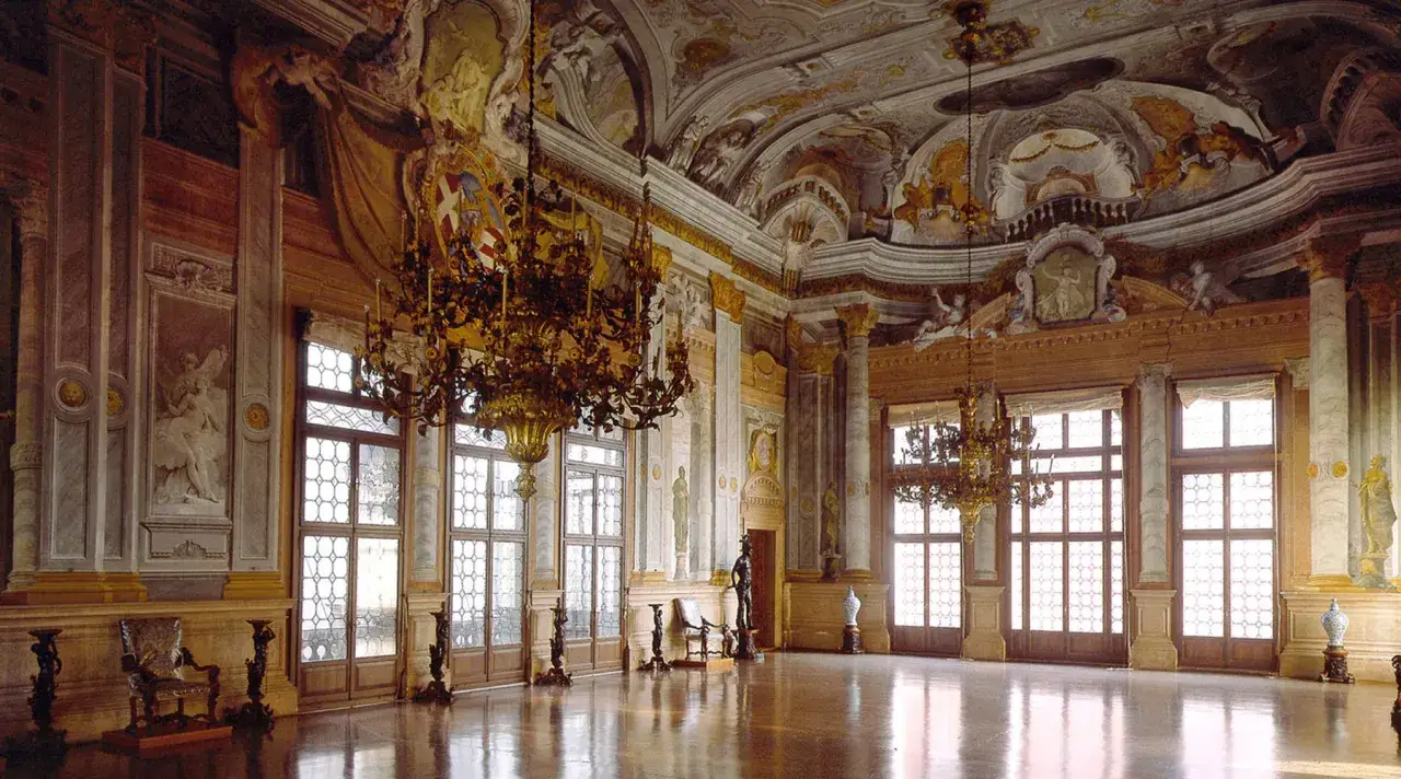 Lussuoso salone del Casino Venier, con lampadari dorati, affreschi sul soffitto e grandi finestre che illuminano il pavimento lucido.