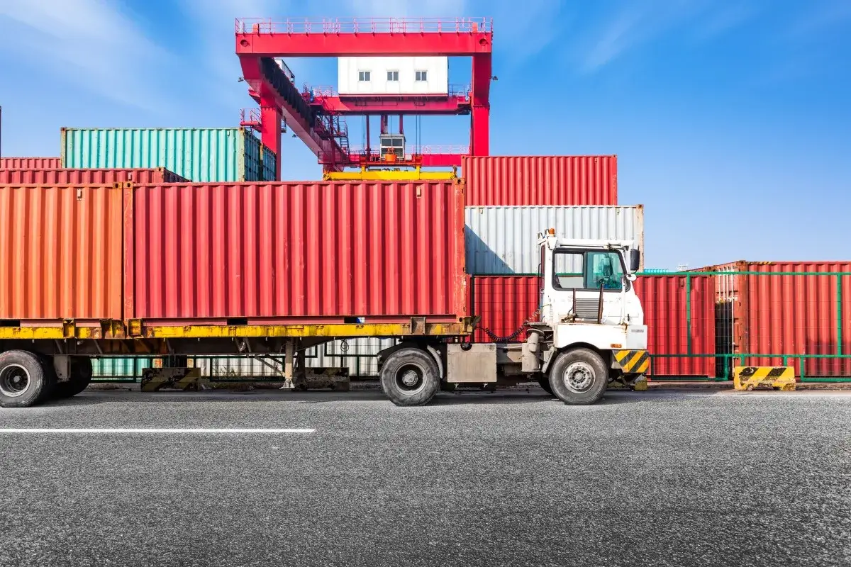 Ciężar&oacute;wka z kontenerami na placu przeładunkowym. Spedytor, kto to? To osoba organizująca transport.