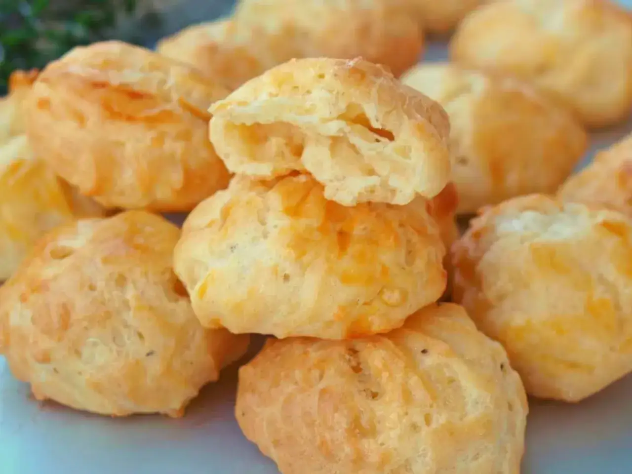 Une pile de goug&egrave;res au fromage dor&eacute;es et moelleuses, certaines coup&eacute;es pour r&eacute;v&eacute;ler leur int&eacute;rieur a&eacute;r&eacute;.