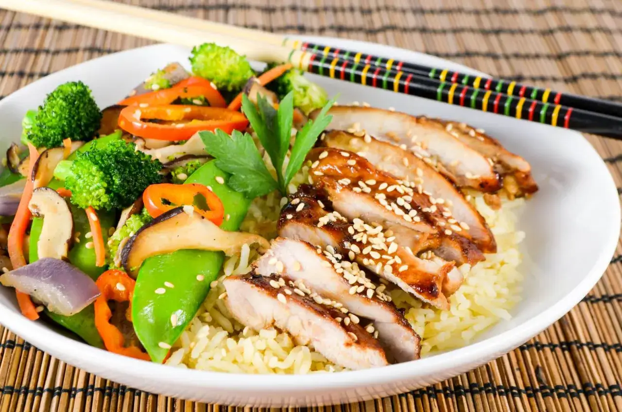 Pyszny teriyaki kurczak z ryżem i kolorowymi warzywami: brokułami, papryką, groszkiem cukrowym i grzybami.