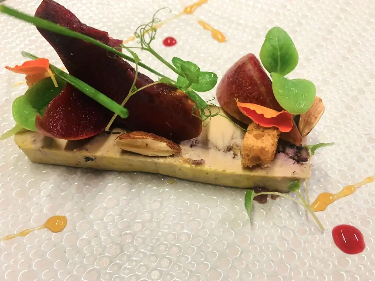 Pressé de foie gras, betterave, amandes et petites pousses vertes, une œuvre culinaire raffinée sur une assiette texturée.