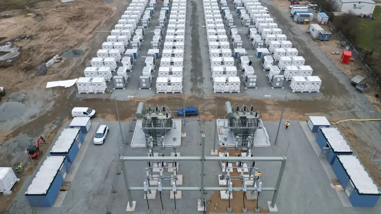 Gro&szlig;e Batterie-Speicheranlage mit vielen wei&szlig;en Containern, die an eine Stromversorgung angeschlossen sind. Ein Blick auf die Zukunft der Energiespeicherung, die auch f&uuml;r Investoren in **Batteriespeicher Aktien** interessant ist.