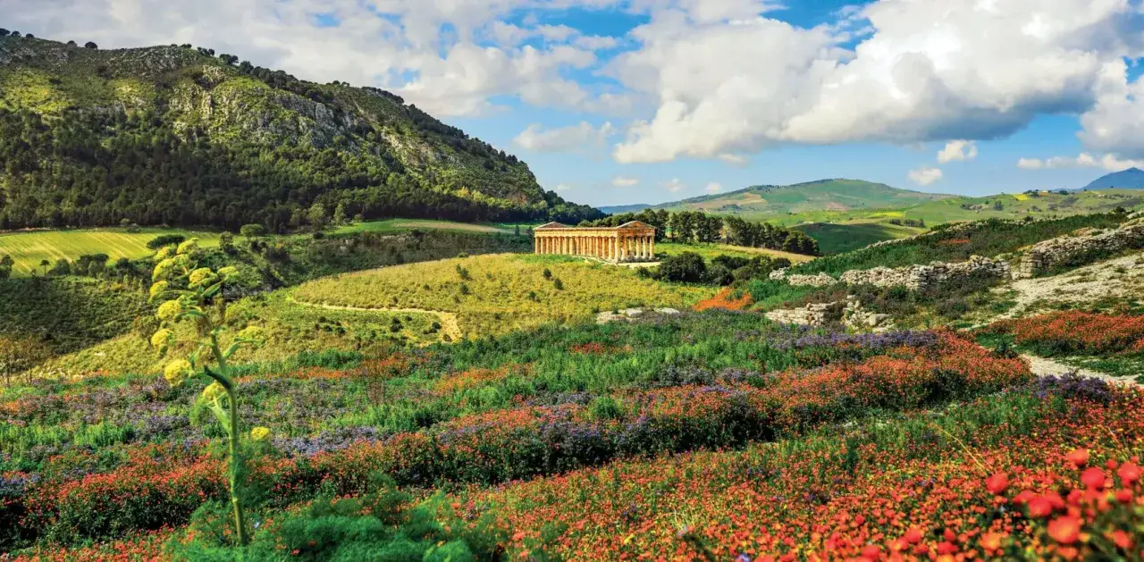 Un temple grec antique se dresse sur une colline verdoyante, entour&eacute; de champs de fleurs sauvages color&eacute;es. Une belle randonn&eacute;e en Sicile.
