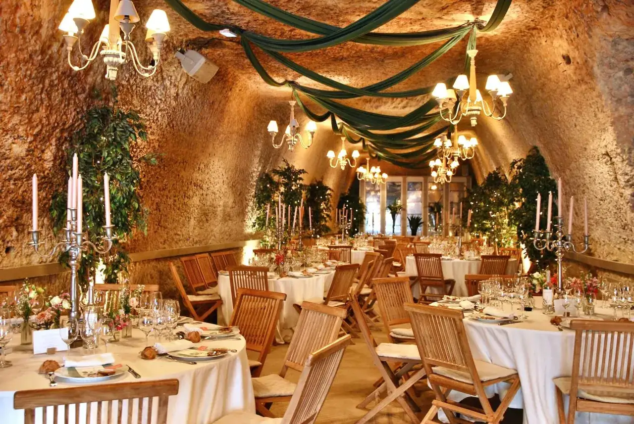 Une salle de r&eacute;ception troglodyte, d&eacute;cor&eacute;e de draperies vertes et de chandeliers, pr&ecirc;te pour une formule pour un mariage.