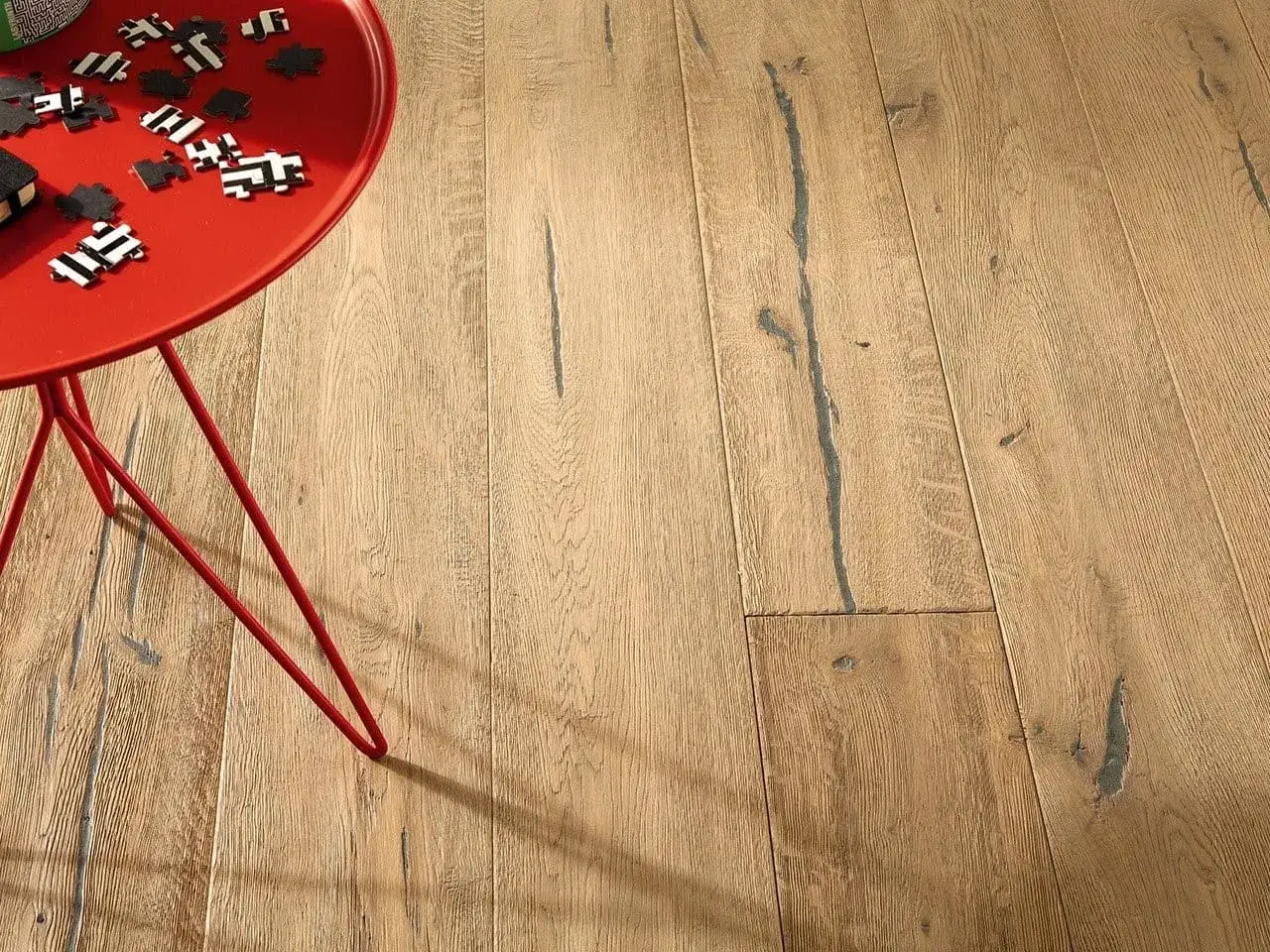 Un tavolino rosso con pezzi di puzzle su un parquet rovere naturale. Scopri come pulire parquet rovere naturale per mantenerlo splendente.
