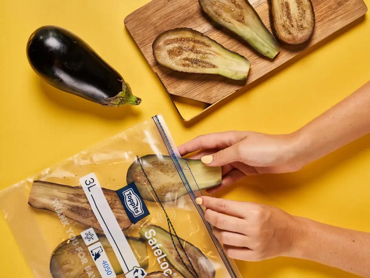 Hände legen Auberginenscheiben in einen Gefrierbeutel. So gelingt das Aubergine einfrieren einfach und platzsparend.