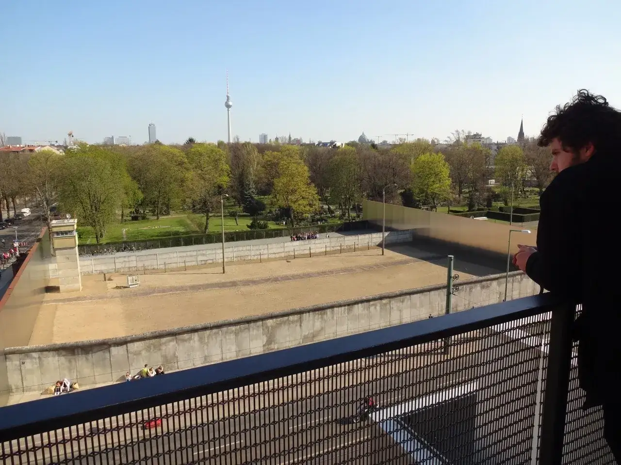 Blick auf ein St&uuml;ck des ehemaligen Berliner Mauer. Ein Mann steht auf einem Balkon und blickt auf die Gedenkst&auml;tte.