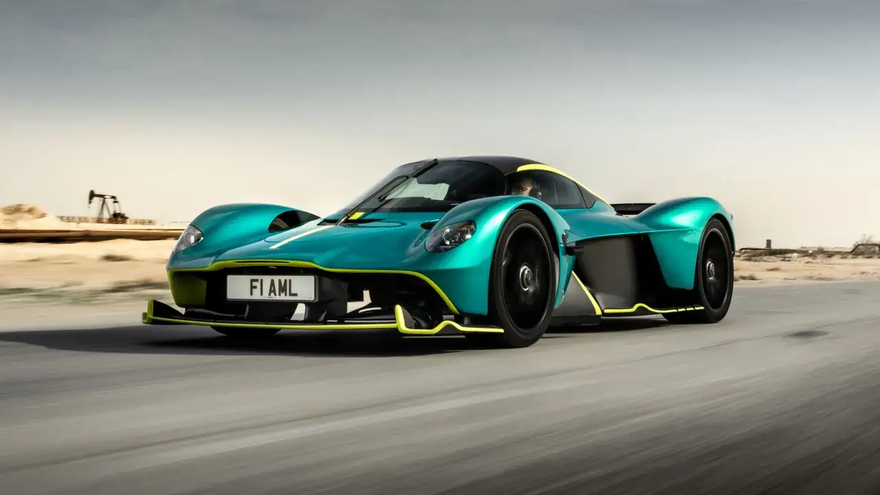 Turkusowy Aston Martin Valkyrie z żółtymi akcentami pędzi po pustynnej drodze, obok widać pompę naftową.