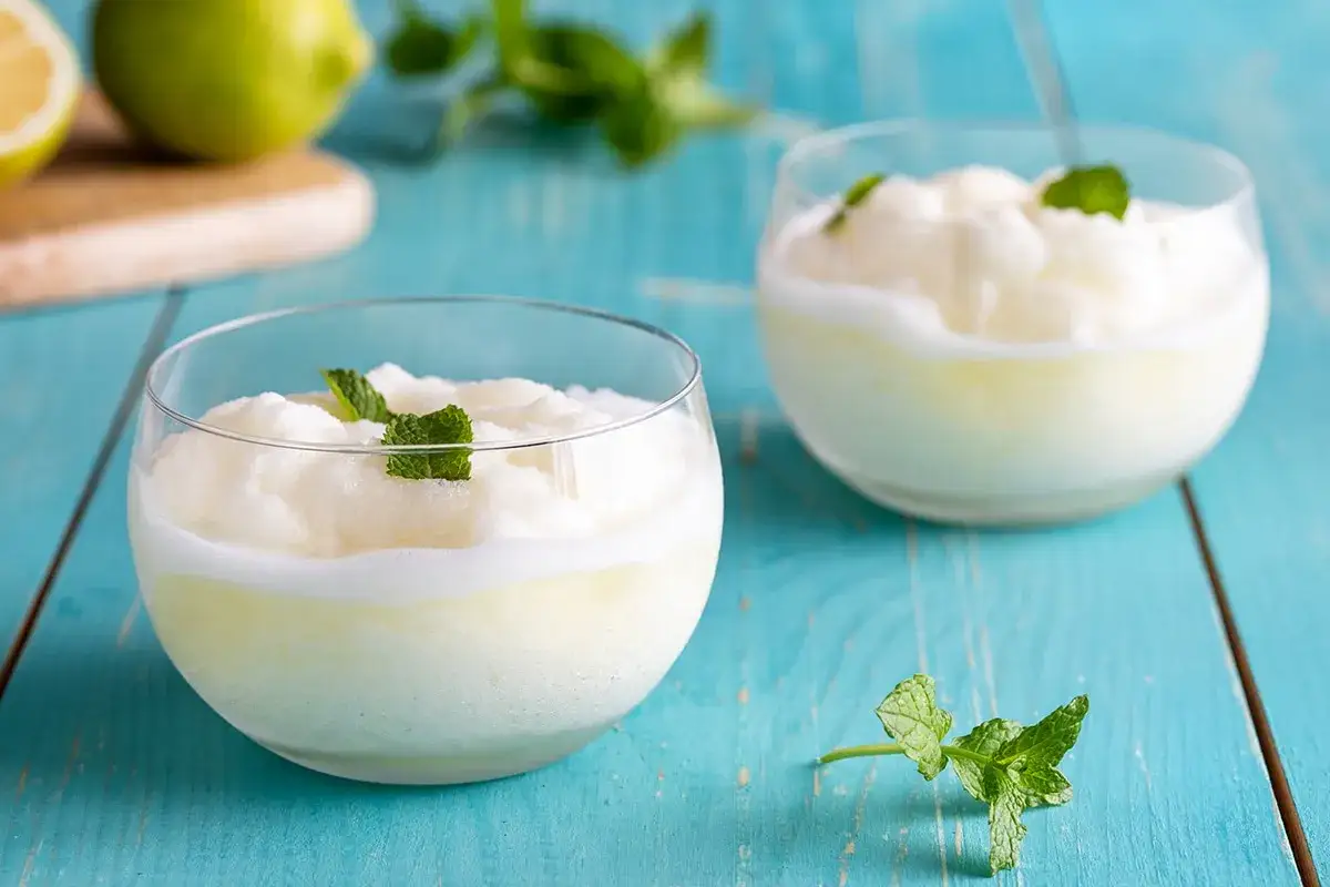 Due bicchieri di sorbetto al limone, guarniti con menta fresca, su un tavolo di legno blu.