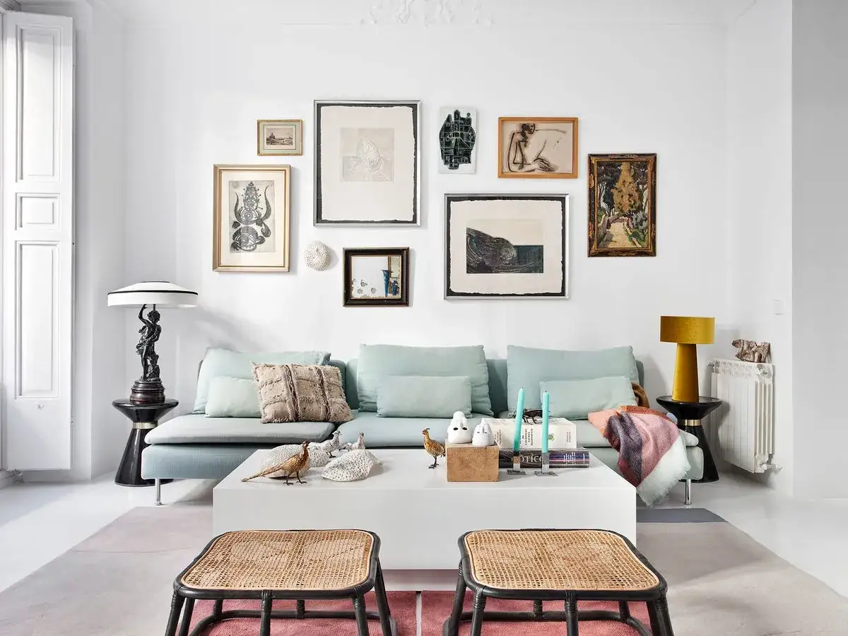 Un sofá azul pálido con cojines decorativos y una colección de arte ecléctica. Ideas de **que poner detras del sofa** para inspirarte.