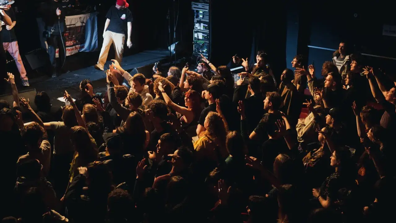 Une foule enthousiaste lève les mains lors d'un concert de rap. L'ambiance est électrique, les artistes sur scène captivent le public.