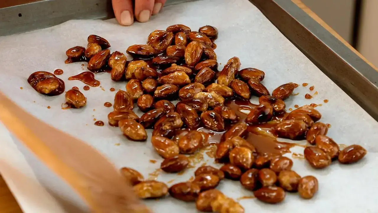 Montón de piñones garrapiñados brillantes y caramelizados sobre papel de horno.