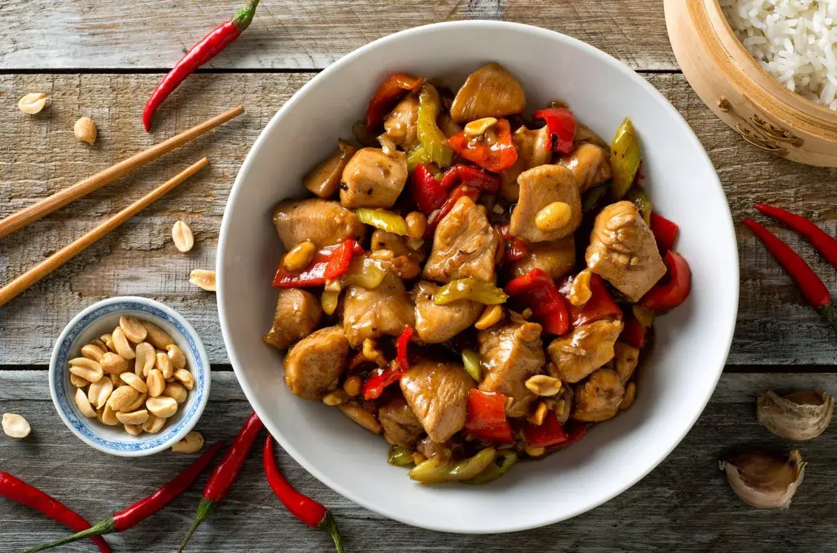 Pyszny kurczak kung pao z papryką, orzeszkami ziemnymi i chili na drewnianym stole.
