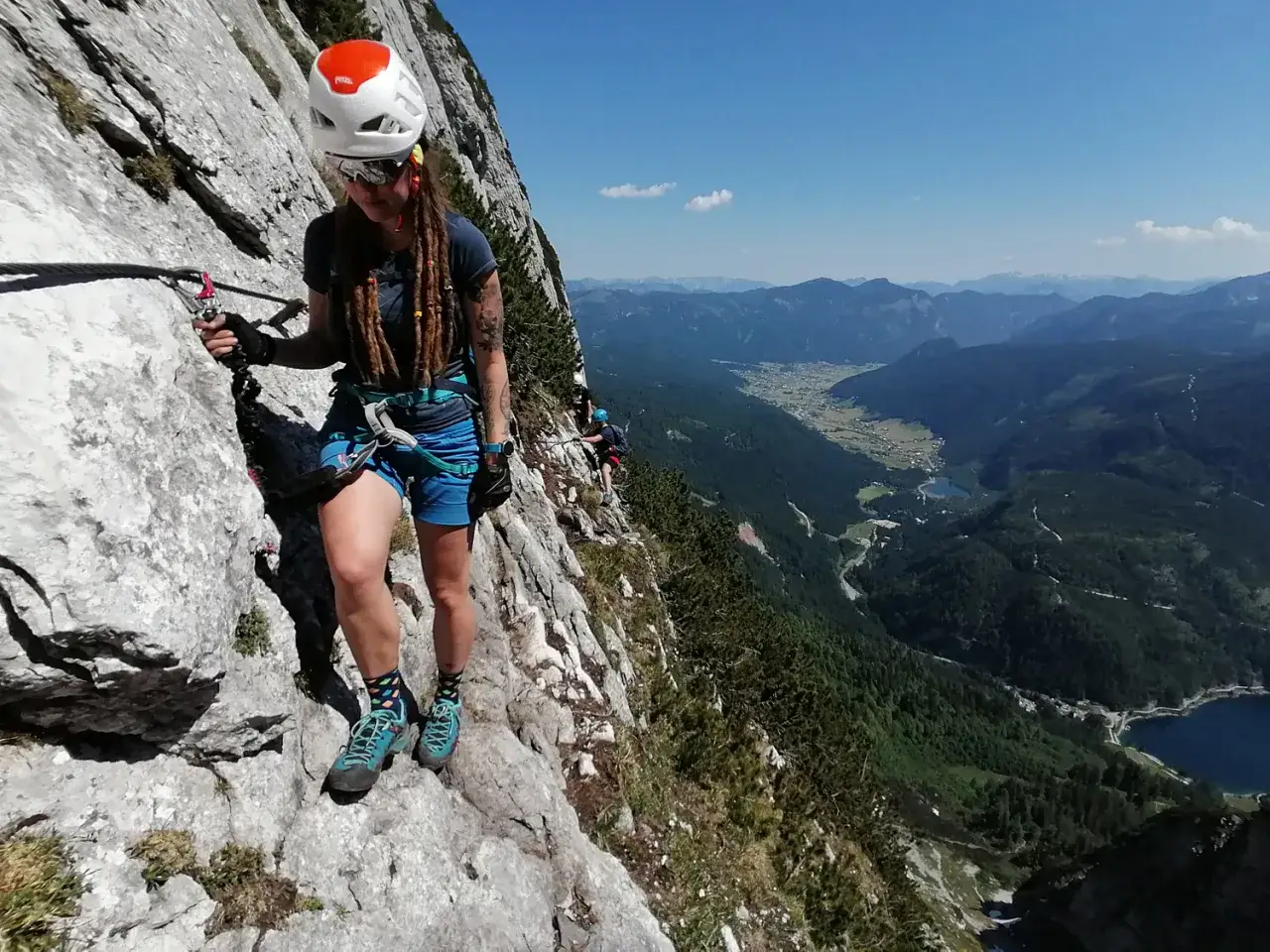 Frau im Klettersteig am Donnerkogel, gesichert am Stahlseil, genie&szlig;t die atemberaubende Aussicht auf das Tal.