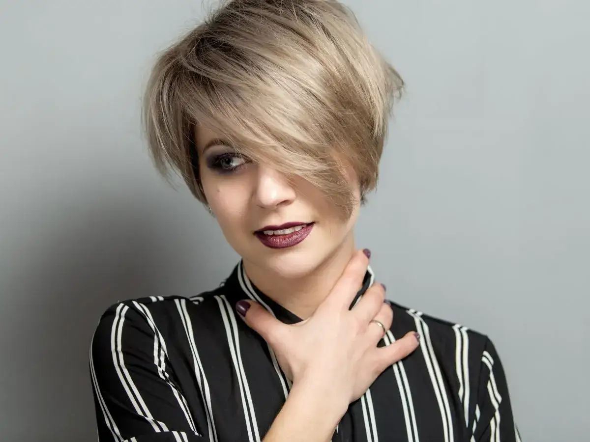 Kobieta z blond pixie bob fryzurą, w bluzce w paski, z ciemną szminką i makijażem oczu.