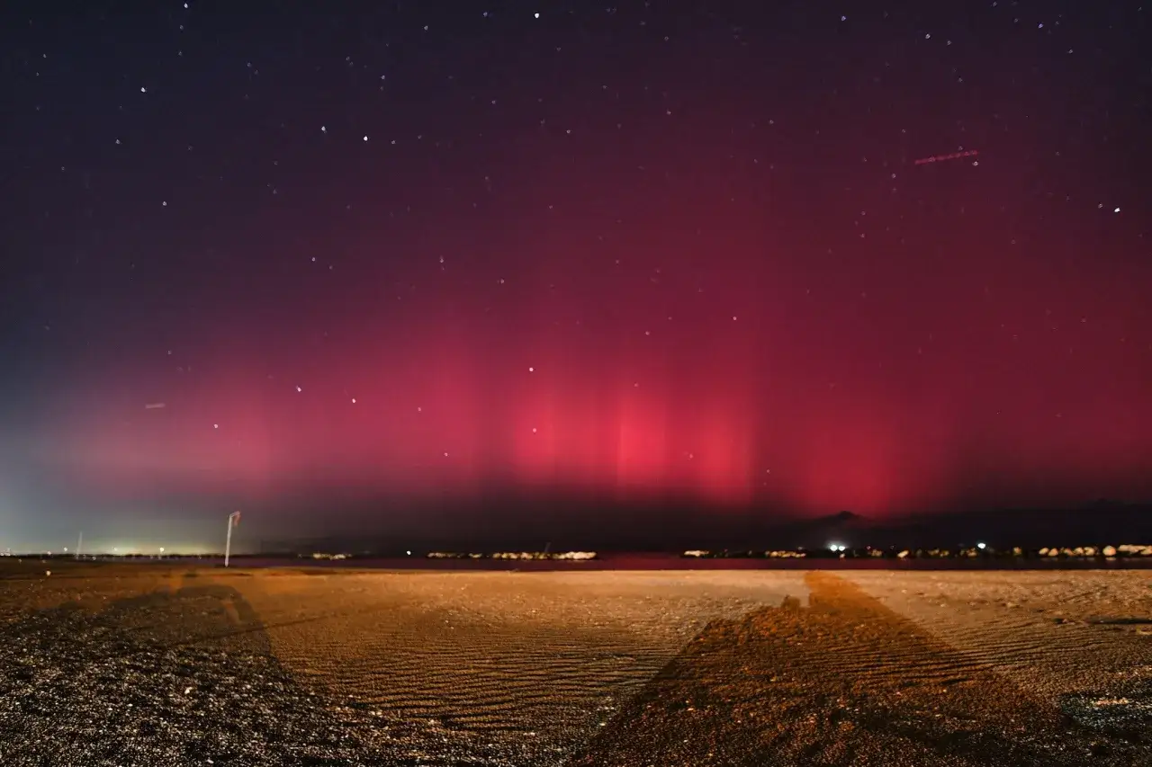 Spettacolo di luci rosse e viola nel cielo notturno, un'incredibile aurora boreale in Italia illumina la spiaggia e il mare.