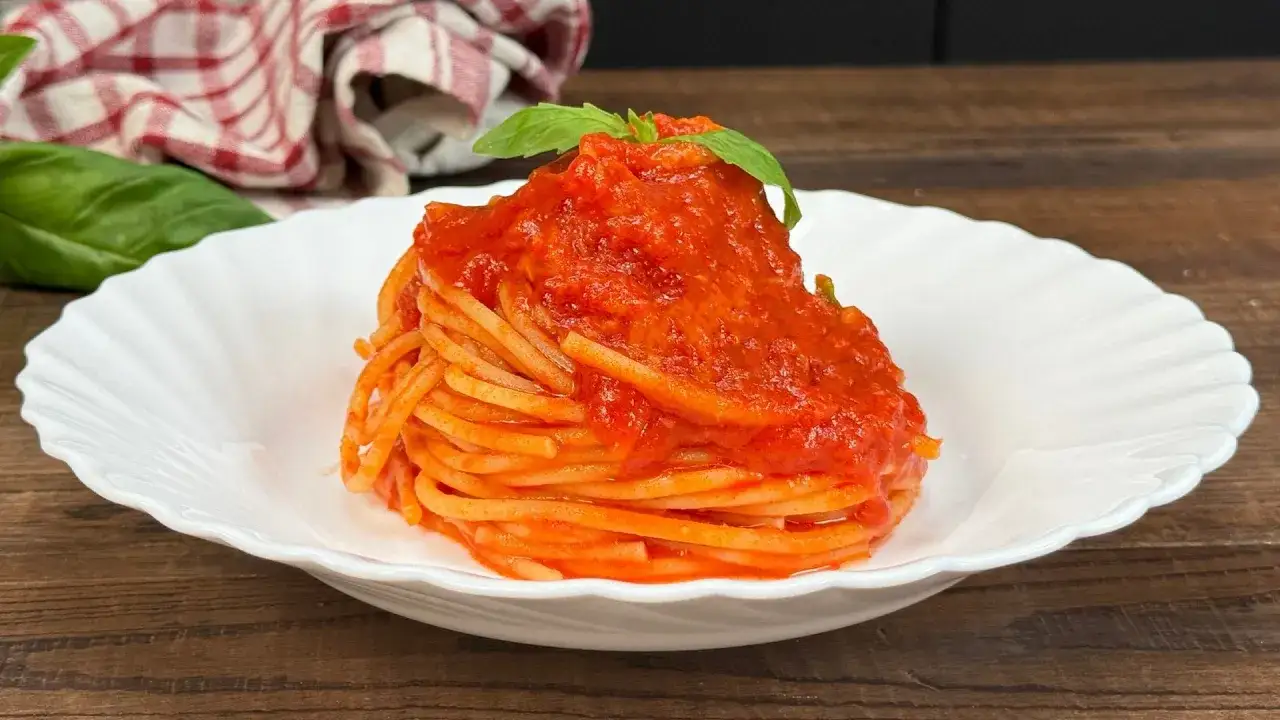 Un piatto di pasta al pomodoro, con spaghetti conditi e guarniti da una foglia di basilico fresco.