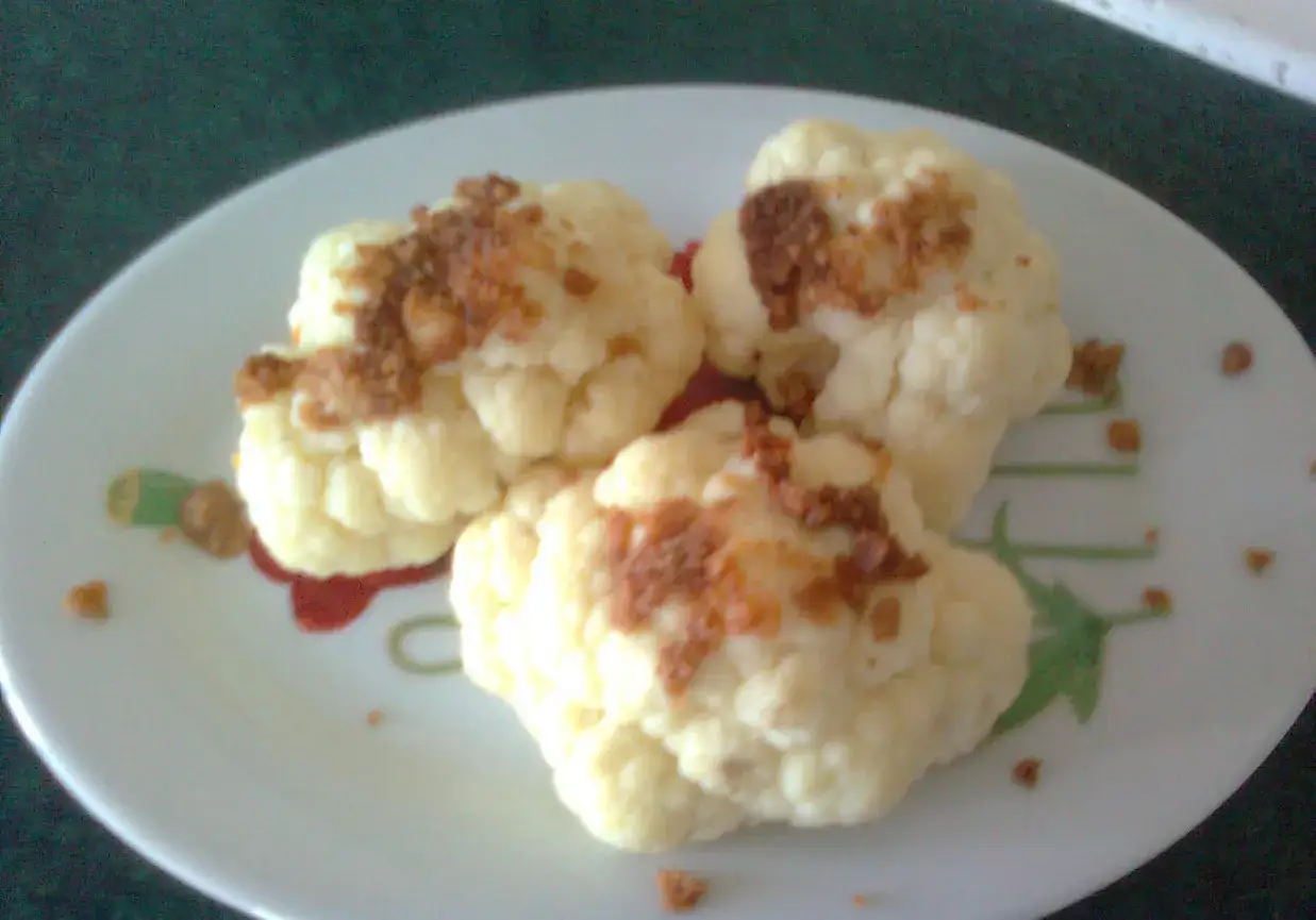Trzy różyczki kalafiora w bułce tartej, podane na talerzu z sosem.