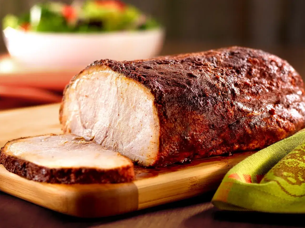 Un jugoso lomo adobado recién horneado, con una rebanada cortada, listo para servir junto a una ensalada fresca.