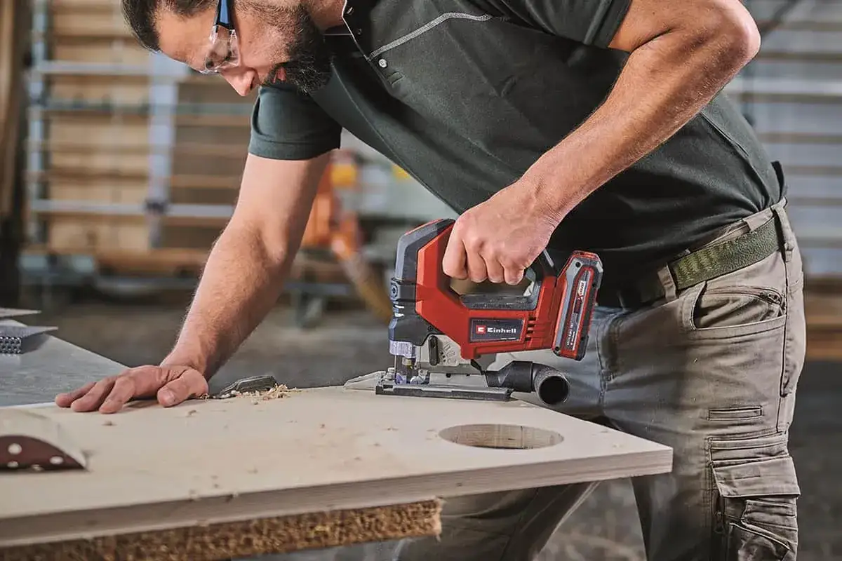Un bricoleur utilise une scie sauteuse sans fil de la marque Einhell pour découper une planche de bois.
