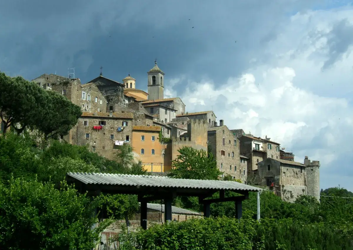 Antico borgo medievale di **Tuscie Vetralla**, con case in pietra e torri che si stagliano su un cielo nuvoloso.