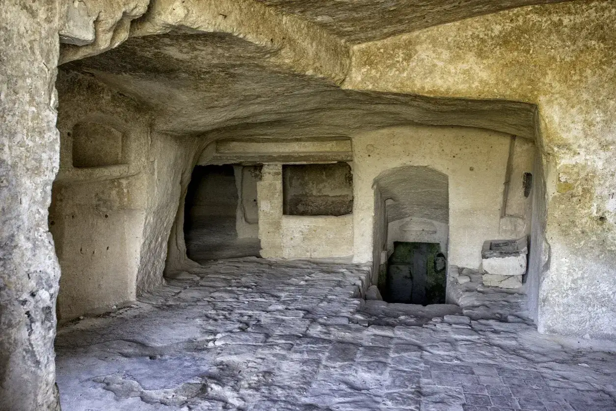 Interno di un'abitazione rupestre nei Sassi di Matera, con pavimentazione in pietra e nicchie scavate nella roccia.