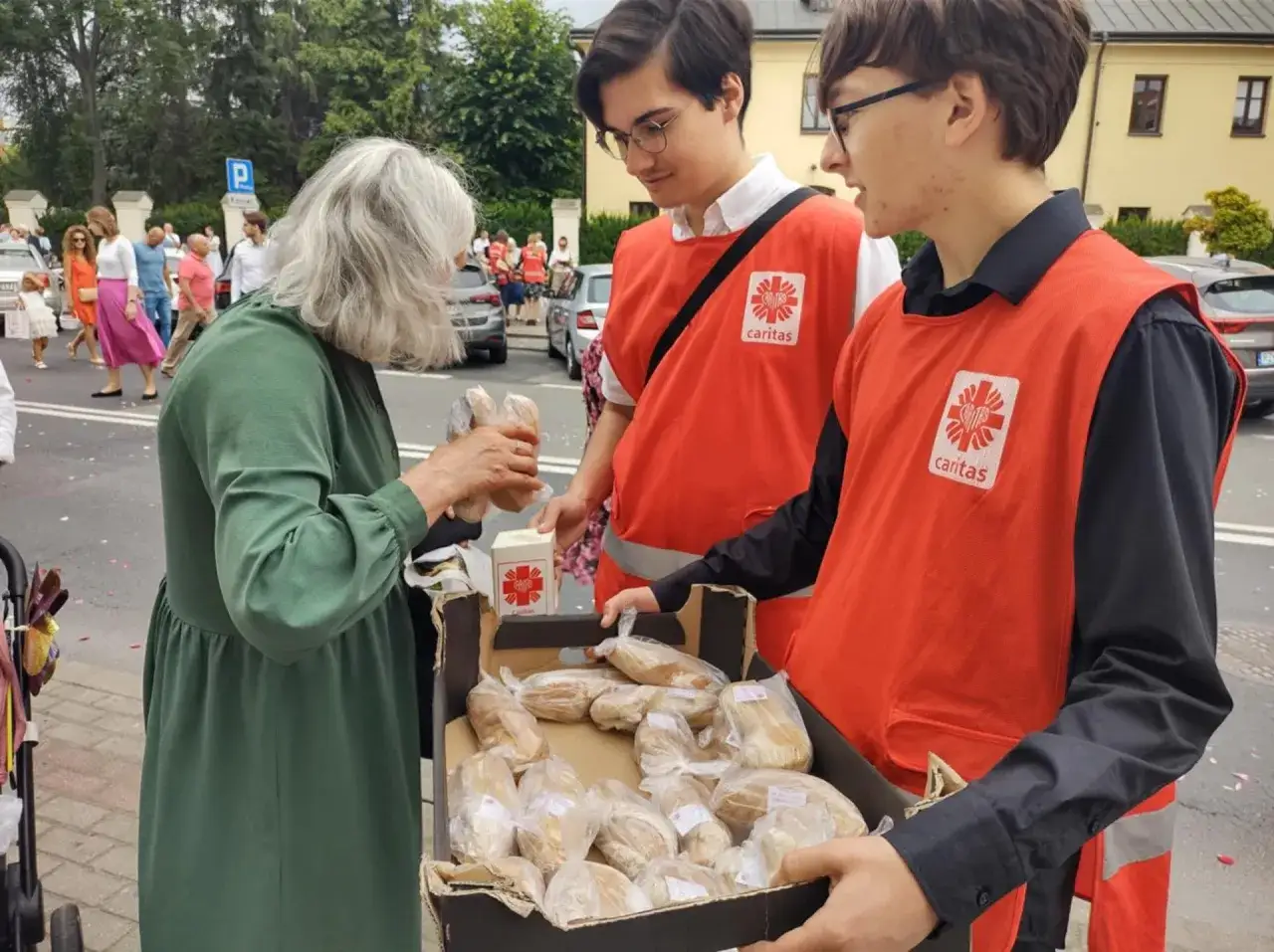 Wolontariusze Caritas rozdają chleb potrzebującym. Starsza pani otrzymuje jałmużnę.