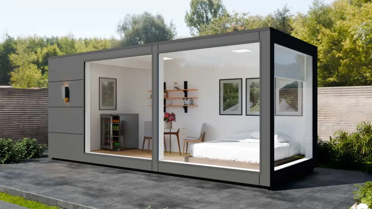 Modernes tiny house container mit Bett, Kühlschrank und Sitzbereich, umgeben von Grün.