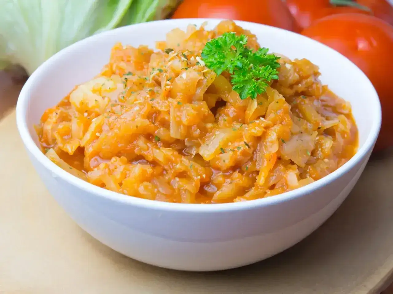 Pyszny bigos ze słodkiej kapusty, duszony z pomidorami i przyprawami, udekorowany natką pietruszki.