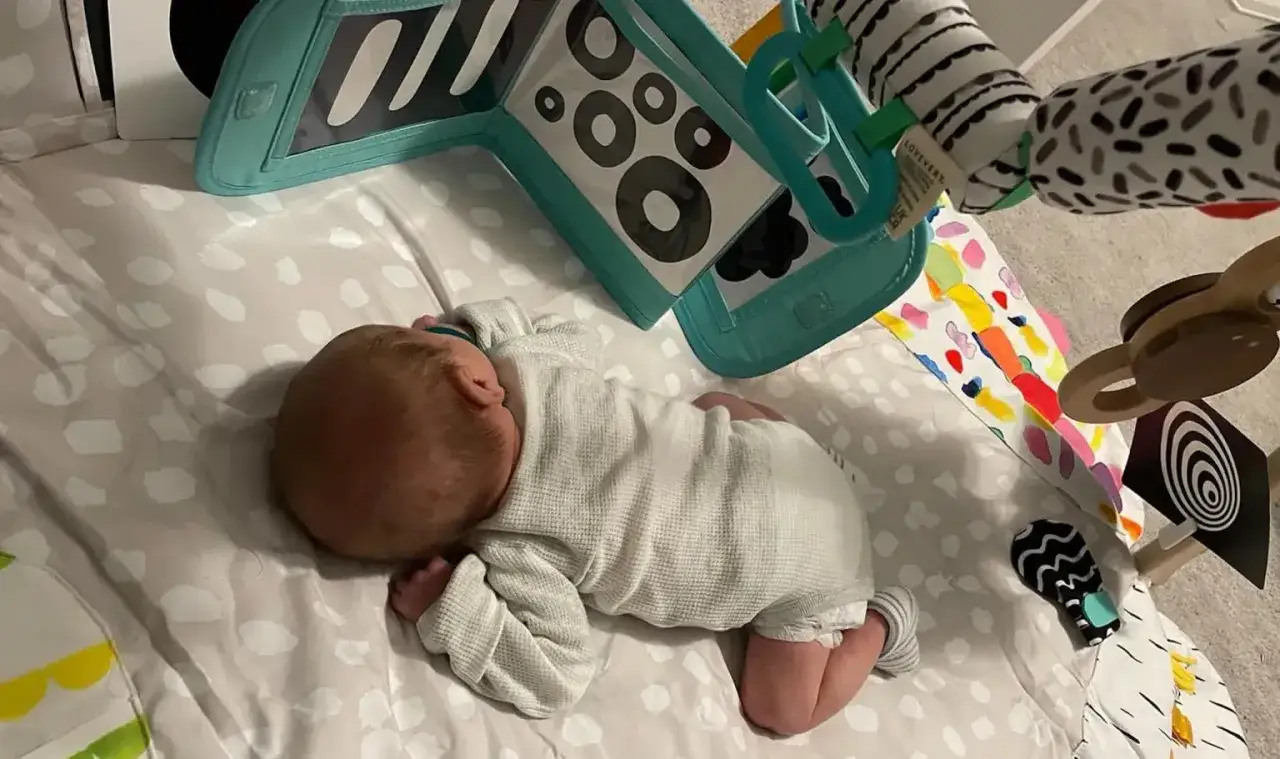 Baby schläft auf Spieldecke, vielleicht im 12 wochen schub. Bunte Spielsachen und Schwarz-Weiß-Muster.