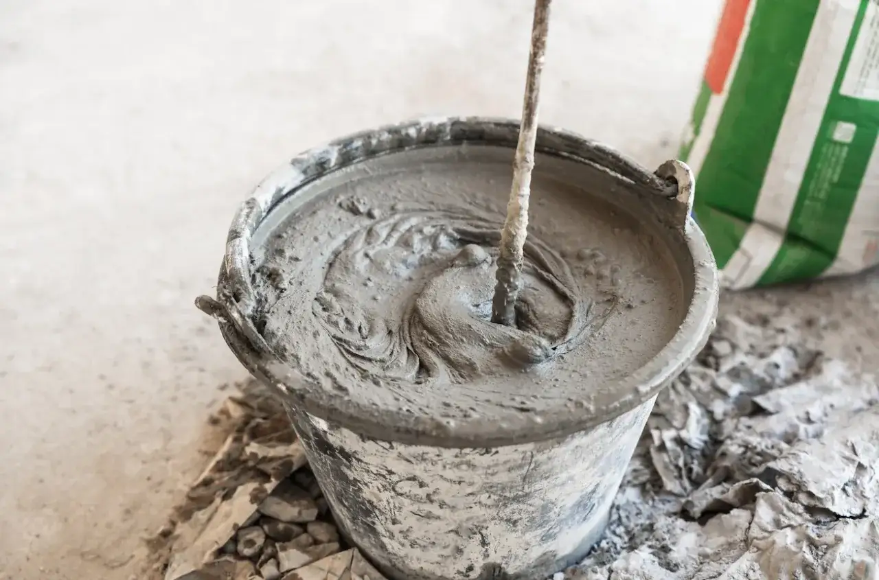 Secchio con malta fresca in preparazione, mostrando la differenza tra malta e cemento. Un sacco di cemento è visibile sullo sfondo.