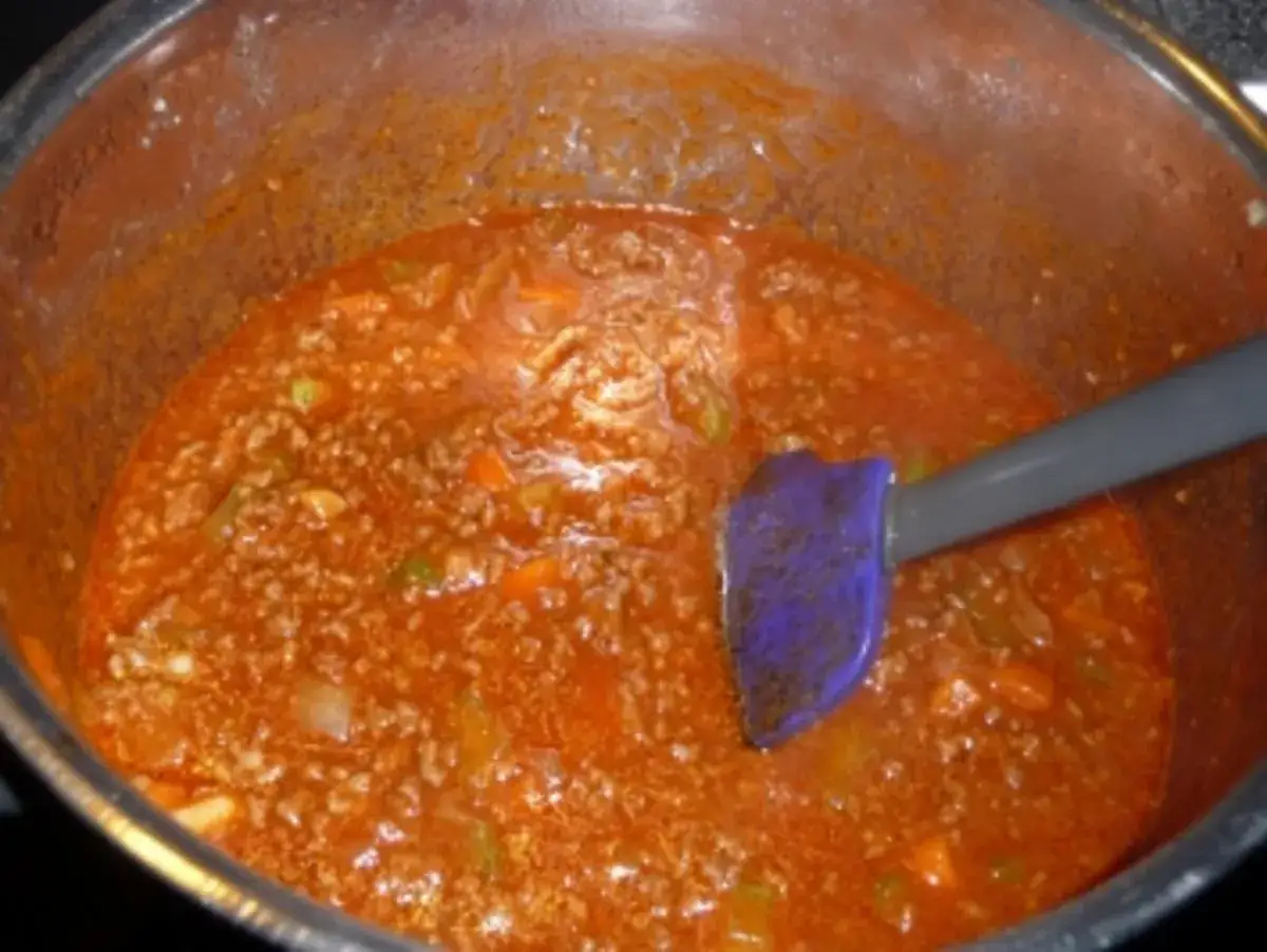 Eine köstliche, **schnelle Bolognese** köchelt in einem Topf. Ein lila Spatel rührt die herzhafte Sauce um.