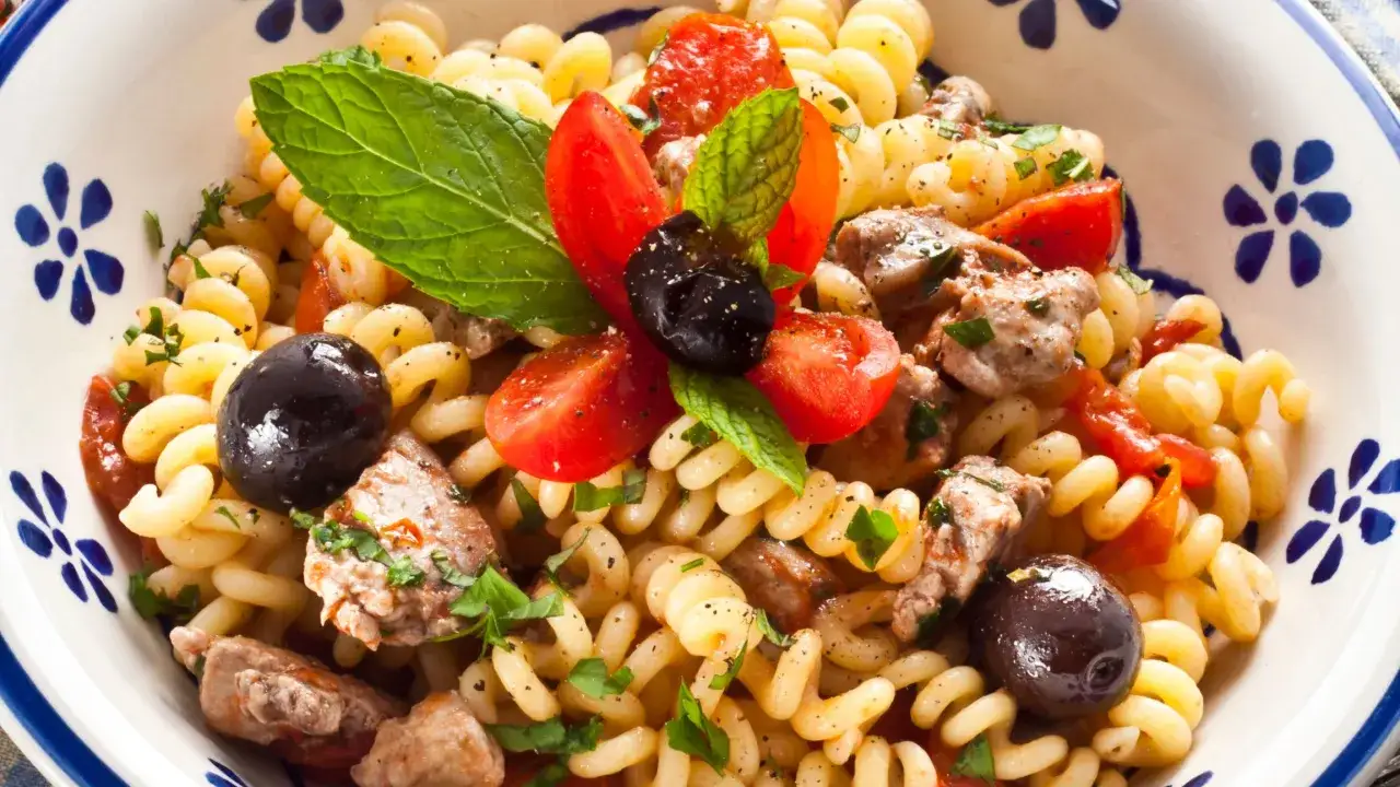 Fusilli con pomodorini, olive nere e pezzetti di pesce spada, guarnita con menta fresca e prezzemolo.