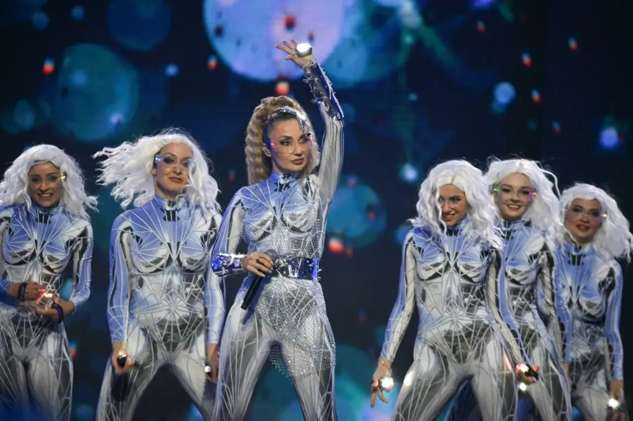 Cleo w futurystycznym stroju z tancerkami na scenie.